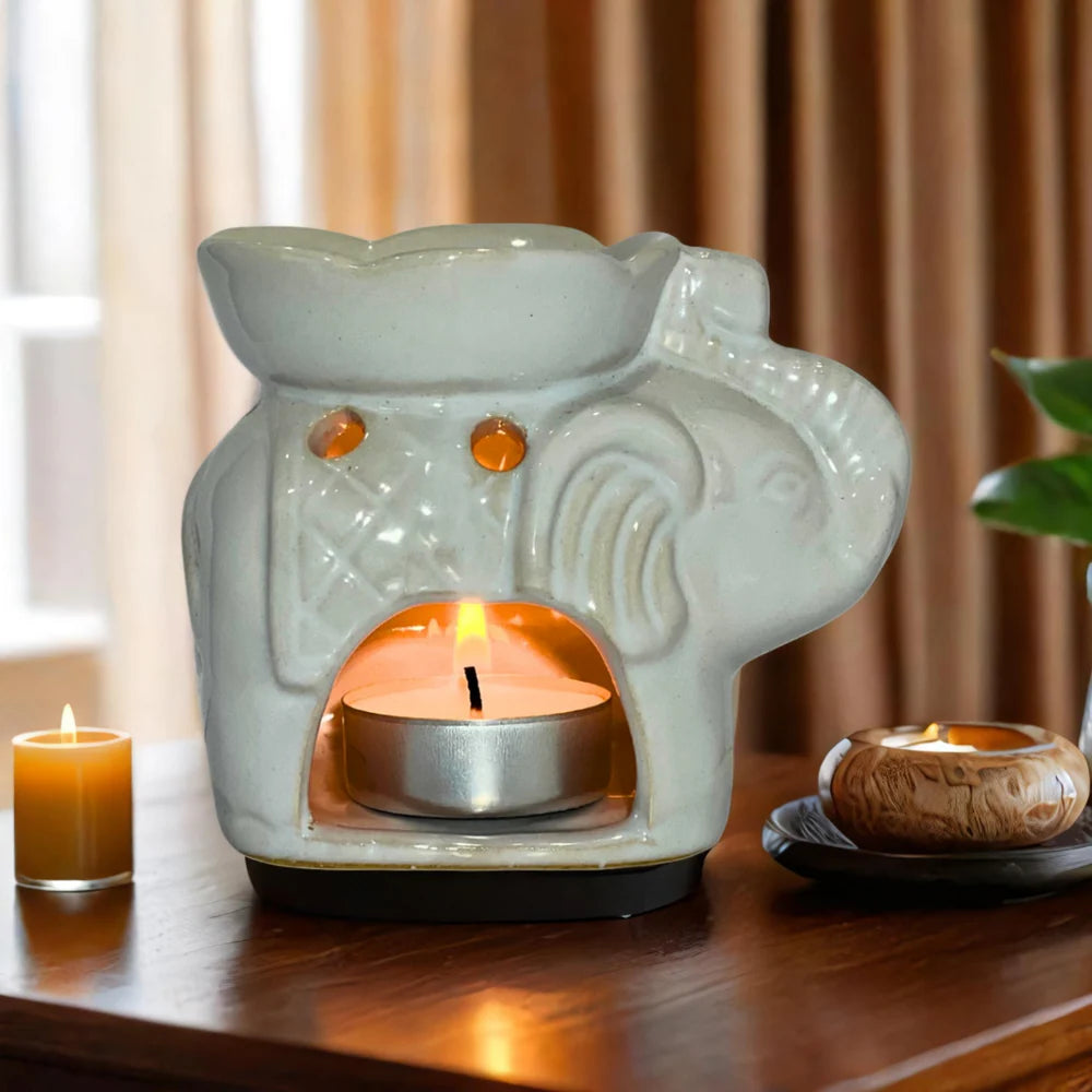 Ceramic wax warmer with a lit candle inside on a wooden surface.