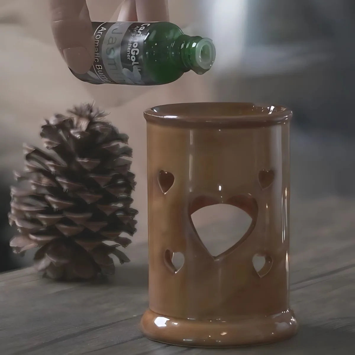 Demonstration of pouring Casino Gold fragrance oil into a ceramic burner with pinecone décor